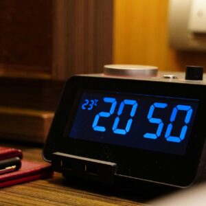 Close-up of a digital alarm clock displaying 20:50 and temperature on a wooden desk with a notepad.