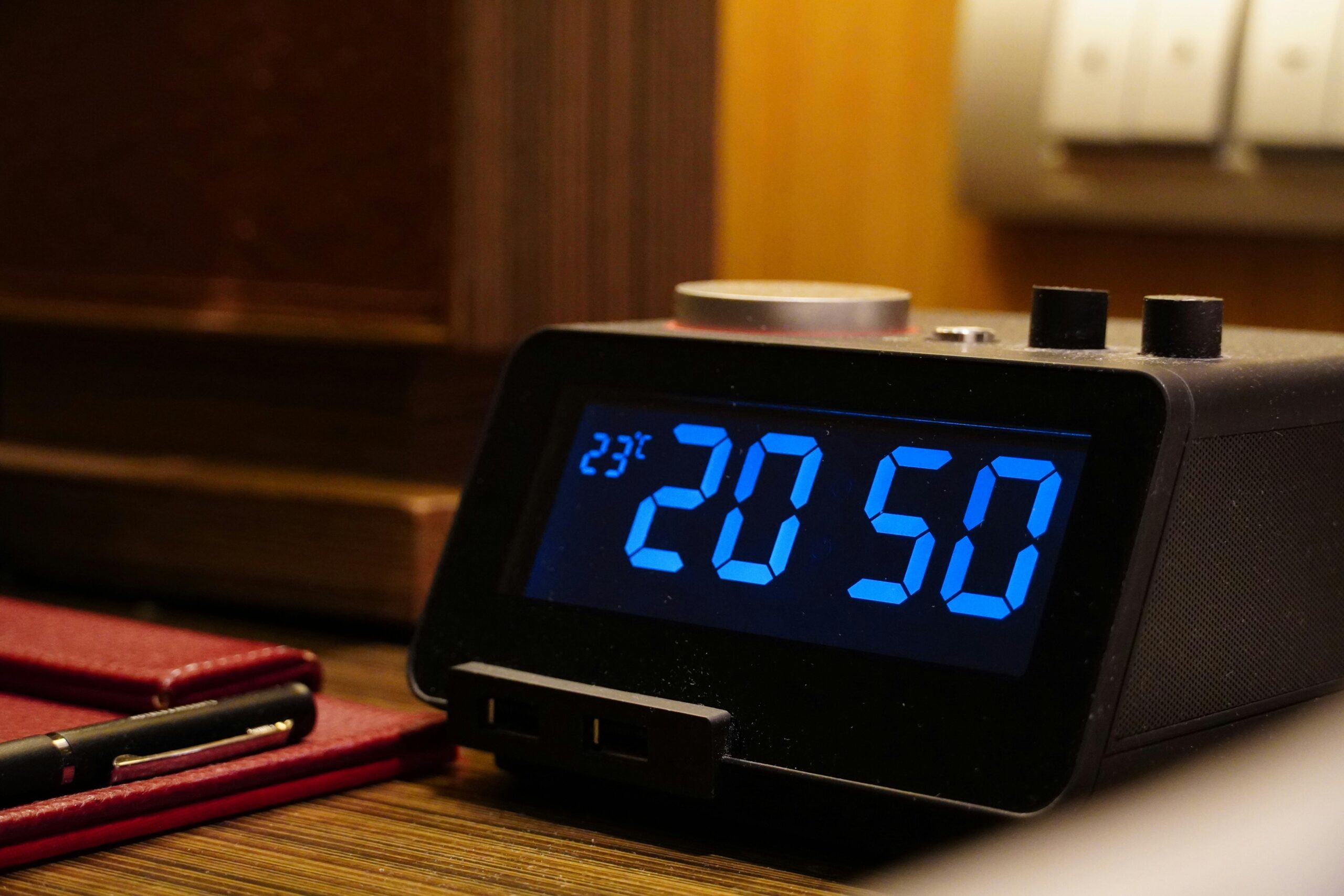 pexels photo 20383452 20383452 Close-up of a digital alarm clock displaying 20:50 and temperature on a wooden desk with a notepad.